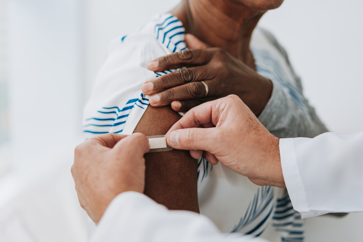 Pair of hands sticking a bandage over flu shot area on woman's shoulder