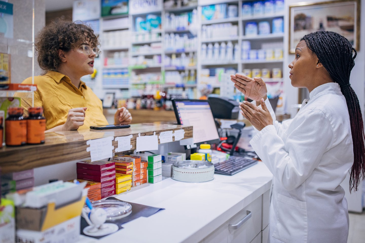 Two dark skinned women having a conversation inside a pharmacy