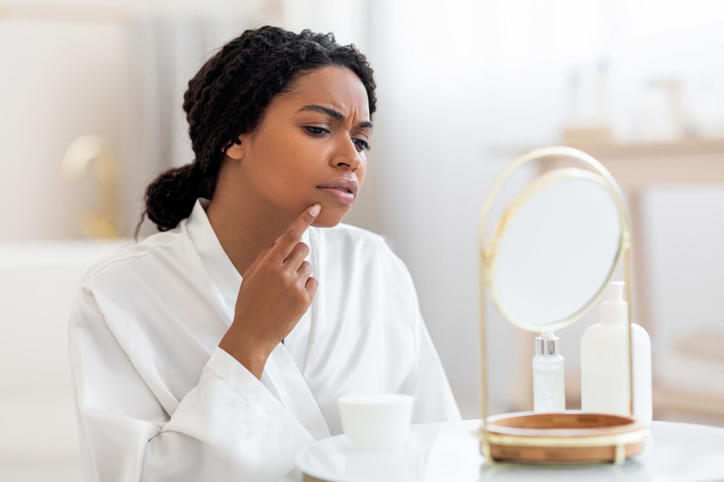 Dark-skinned woman touching her acne as she looks in the mirror