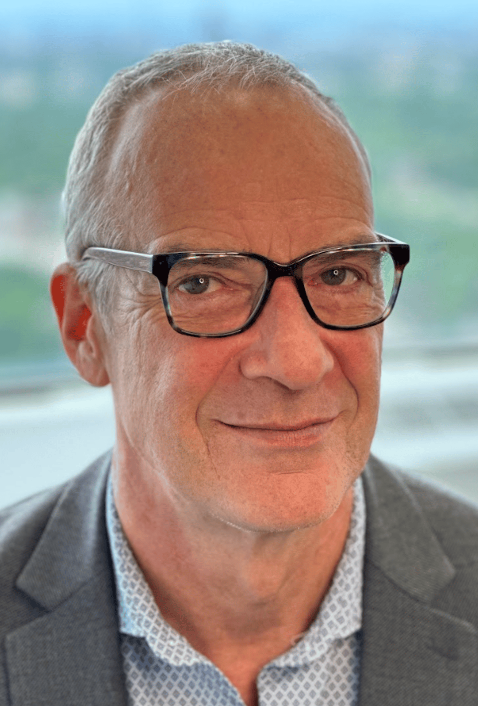 Medical Post Editor in Chief Colin Leslie wearing a grey suit and glasses smiling for a photo