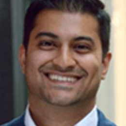 a man wearing a suit and tie smiling at the camera