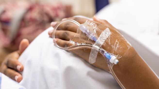 Black woman's hand with IV cradling baby bump in hospital