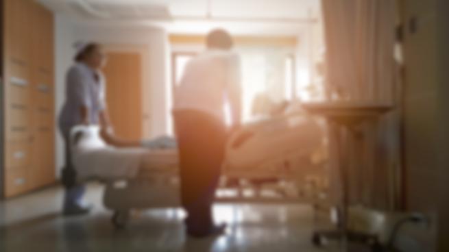 Blurry wides shot of a hospital room with a doctor leaning over a patient