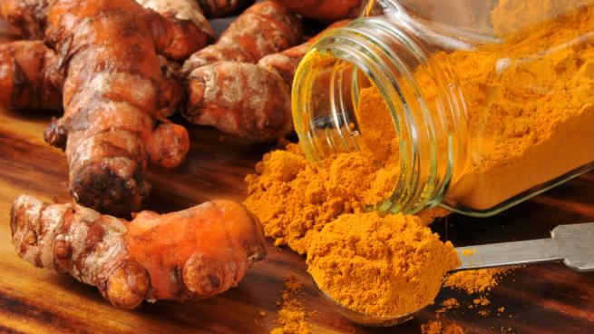 Close up of turmeric root and turmeric powder coming out of clear jar, bright orange colour