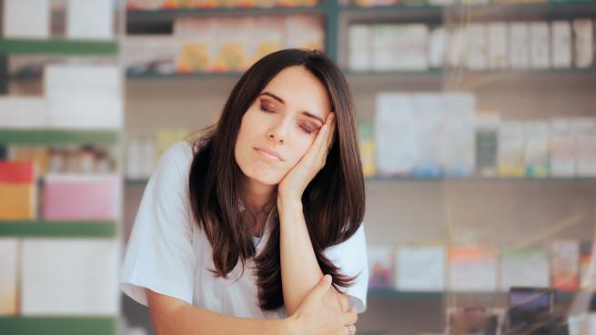 Young white woman pharmacist standing at the counter looking sleepy