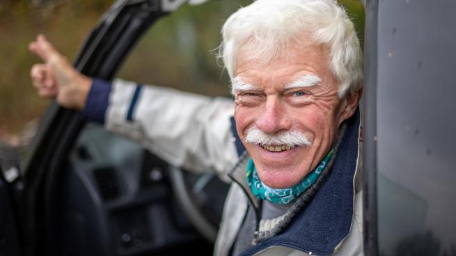 Older white man looking back and smiling from the driver's seat of a sedan