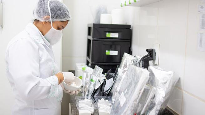 a professional pharmacy worker wearing protective clothing and a mask is compounding medications